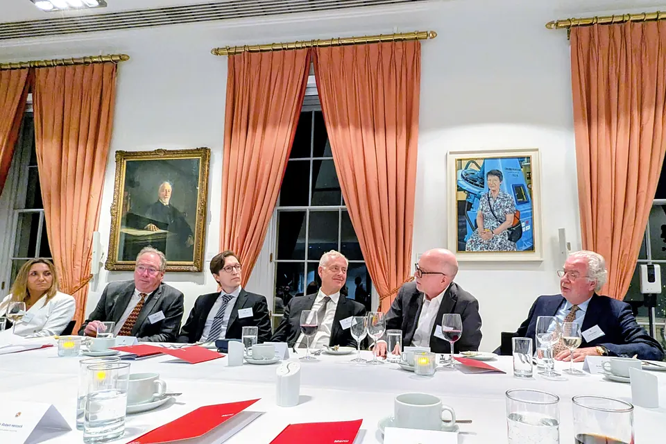 Guests seated along the dinner table in a room with tall windows, salmon-coloured curtains and portraits on white walls.