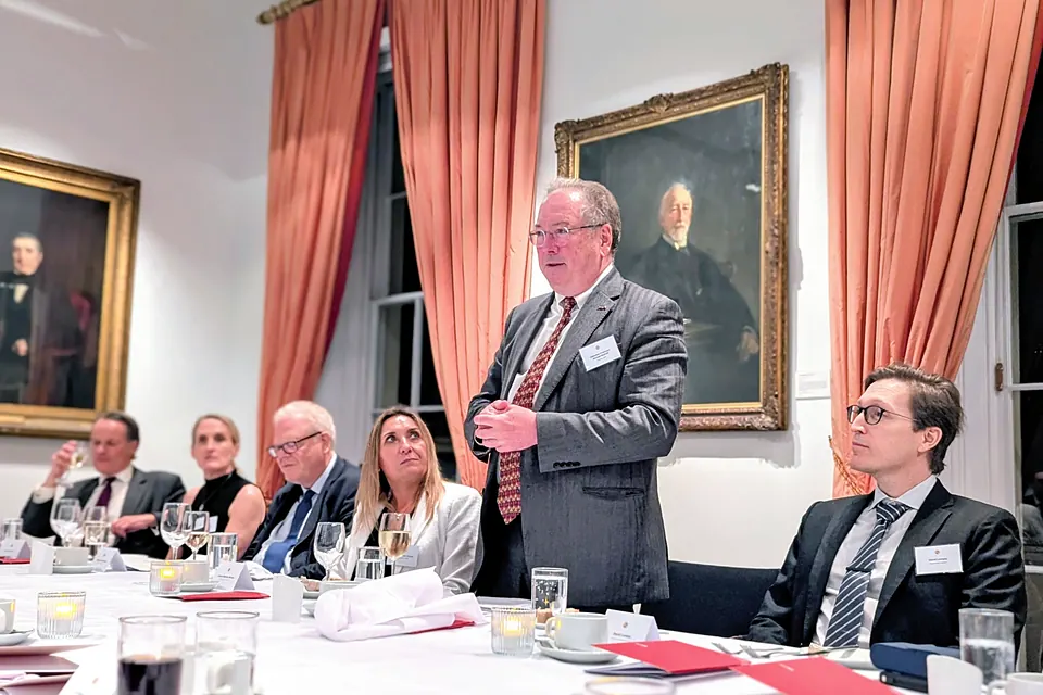 Michael Mainelli stands to address the table, hands clasped, beneath a portrait; seated guests look up to listen.