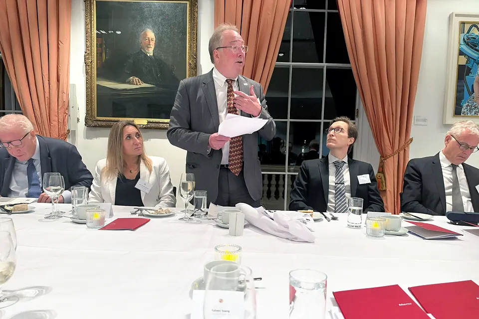 Michael Mainelli stands holding notes and addresses the table, with seated guests on either side.