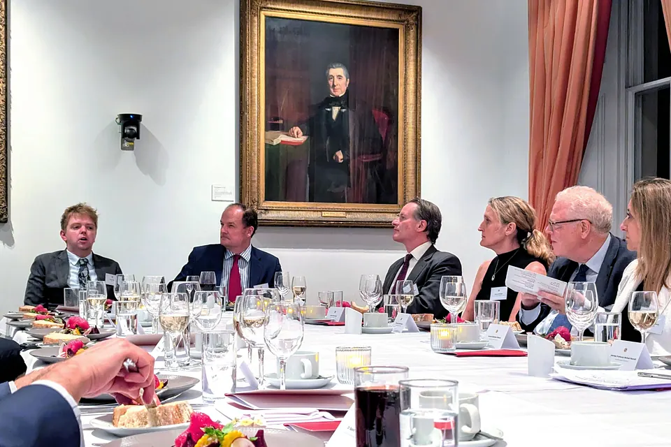 Six guests at the table during dinner, beneath a large nineteenth-century portrait.